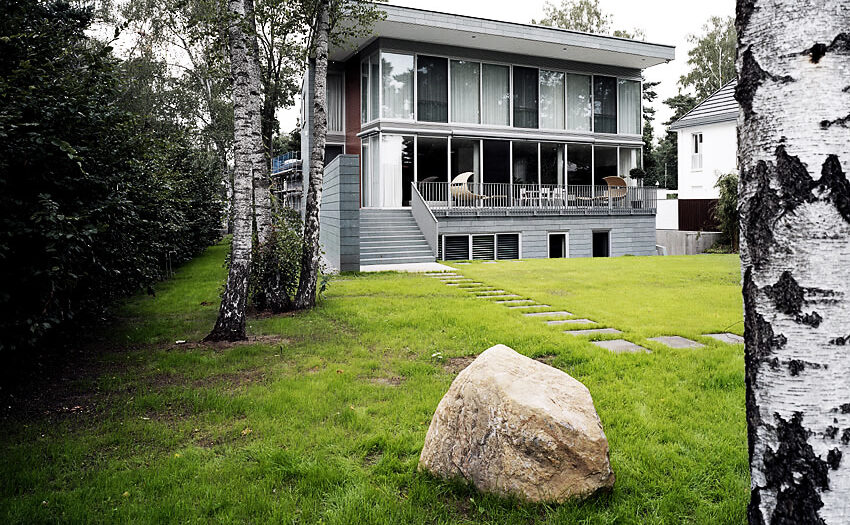 Blick auf Villa mit Terrasse, Terrassentreppe, Trittplatten im Rasen, Findling, Hecke und Birken