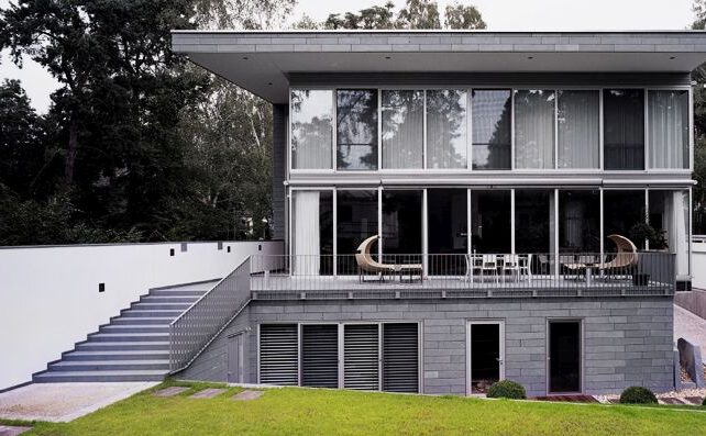 Blick auf Villa mit Terrasse, Terrassentreppe, Trittplatten im Rasen vor waldartigem Hintergrund