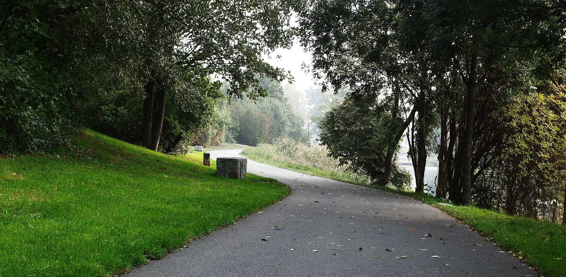 geschwungener, asphaltierter Uferweg mit Granitsitzblöcken zwischen naturnaher Uferbepflanzung